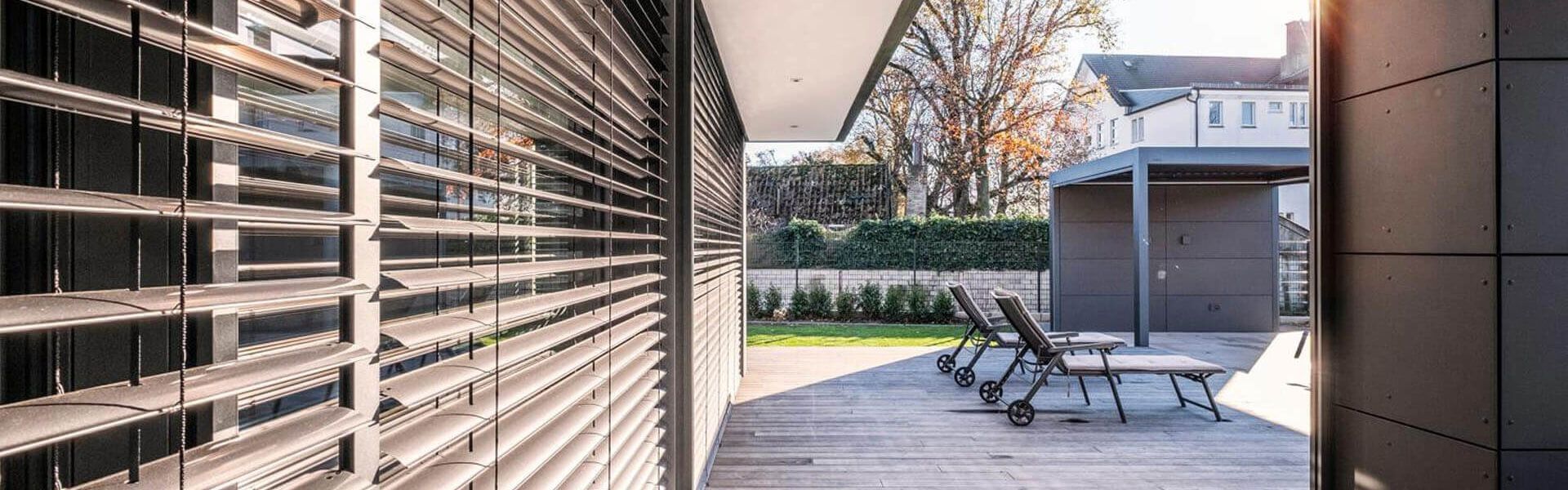 Außenansicht moderner Raffstores an Glasfront mit Blick auf Terrasse und Garten