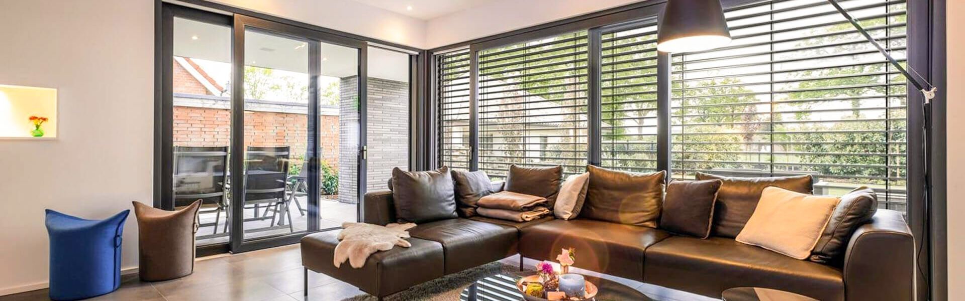 Helles Wohnzimmer mit bodentiefen Fenstern und innenliegenden Raffstores zur Lichtregulierung